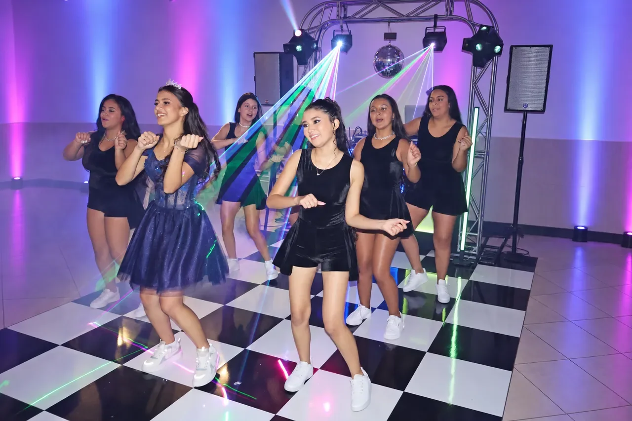 Alice e as amigas durante uma coreografia com iluminação e efeitos de laser.