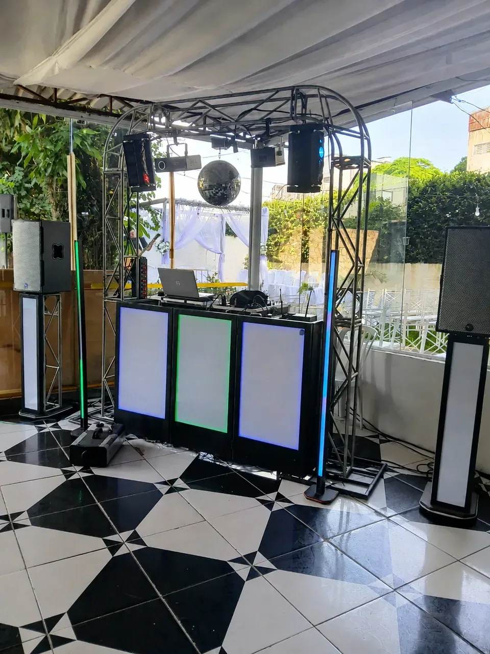 Montagem para evento durante o dia. Treliça, cabine, globo espelhado e caixas de som instalados em salão com luz natural.