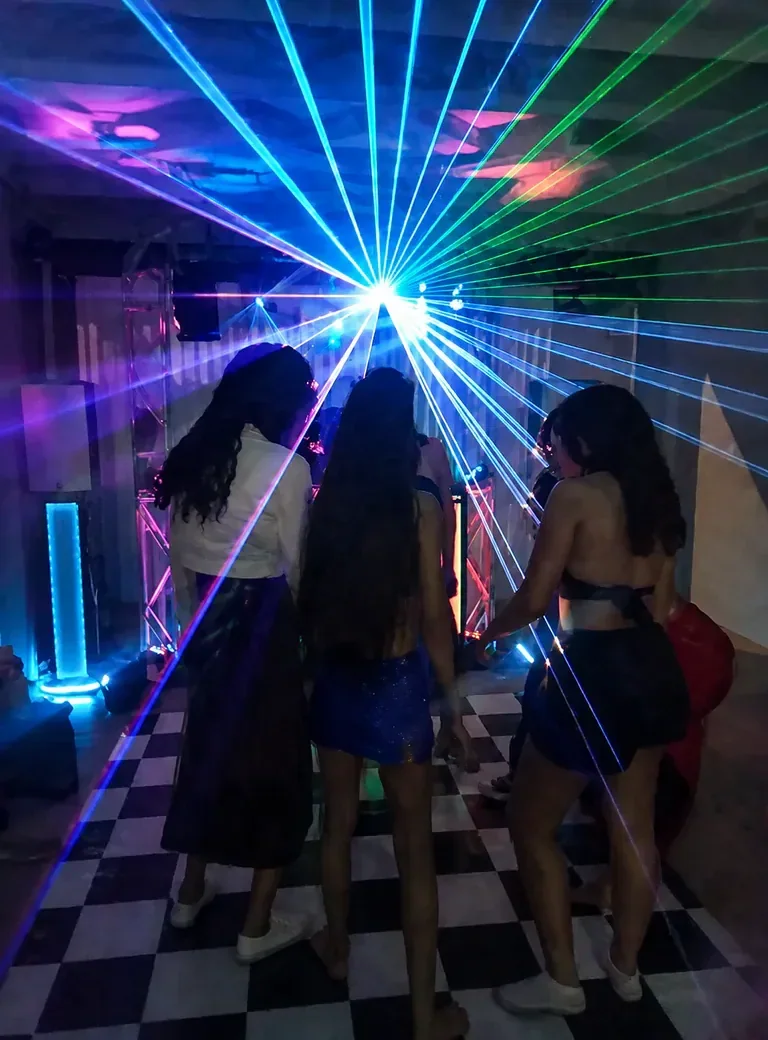 Dança sob laser em pista xadrez. Grupo de convidados aproveitando a seleção do DJ em uma pista marcada por feixes de luz intensos.