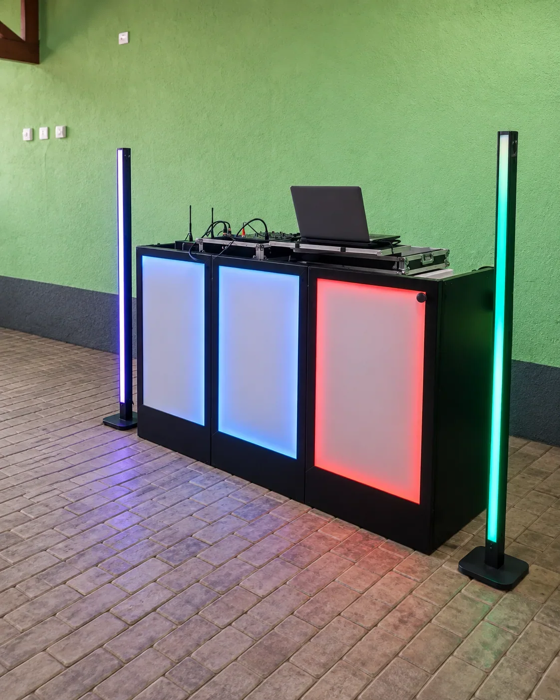 Cabine de DJ com três painéis iluminados, notebook e duas barras verticais de luz