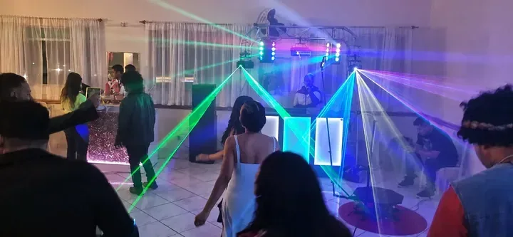 Pista animada com laser colorido. Convidados dançando diante da cabine do DJ com feixes de laser verde, azul e violeta durante a festa.